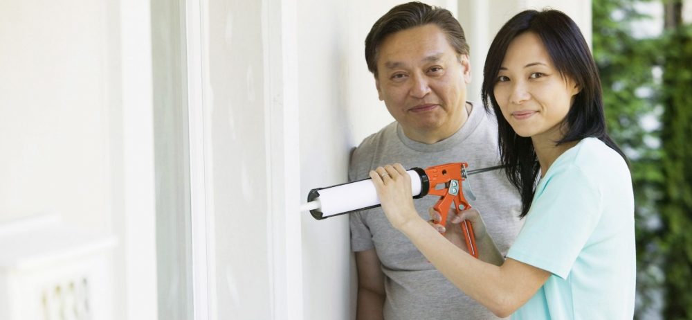 Mid adult man standing with a young woman using a caulk gun