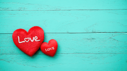 Two read hearts with the word "love" written inside of them on a wooden blue background